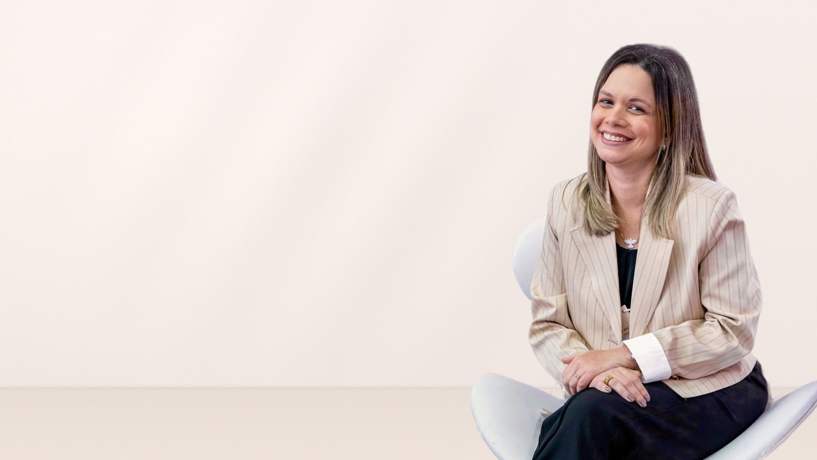 Marcella Campos, nutricionista, sorrindo, sentada em uma cadeira branca, de blazer claro
